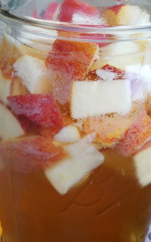 Close up view of a mason jar filled with Autumn Hard Apple Cider Sangria and chopped apples.