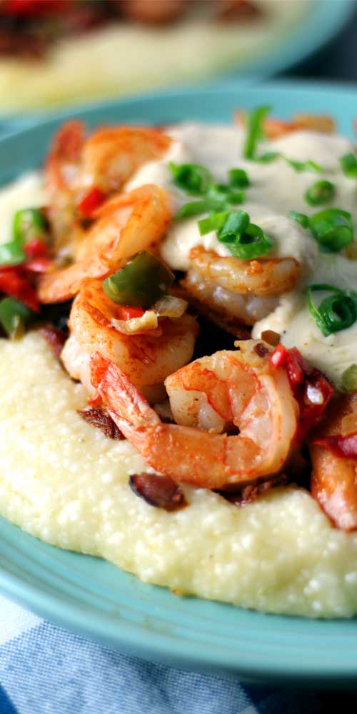 Close up view of Shrimp and Grits on a blue plate. The dish has been garnished with green onion.