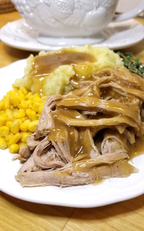 A white plate with corn, Trisha Yearwood’s Crock Pot Pork Tenderloin, and mashed potatoes and gravy.