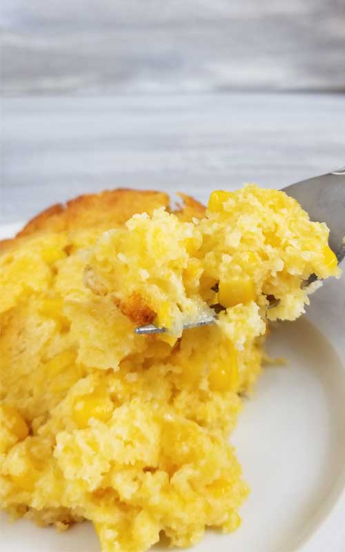A piece of Sweet Creamed Corn Casserole on a white plate. One bite is being held up on a fork.