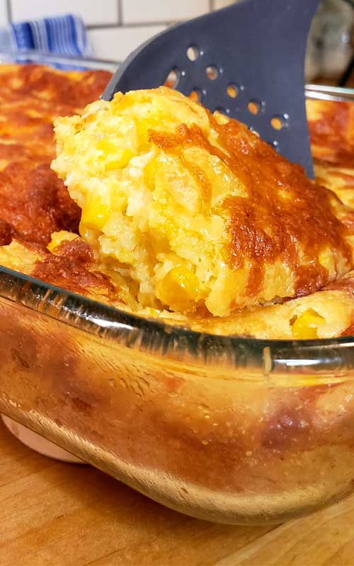 A slotted spoon scooping out some Sweet Creamed Corn Casserole from a glass casserole dish.
