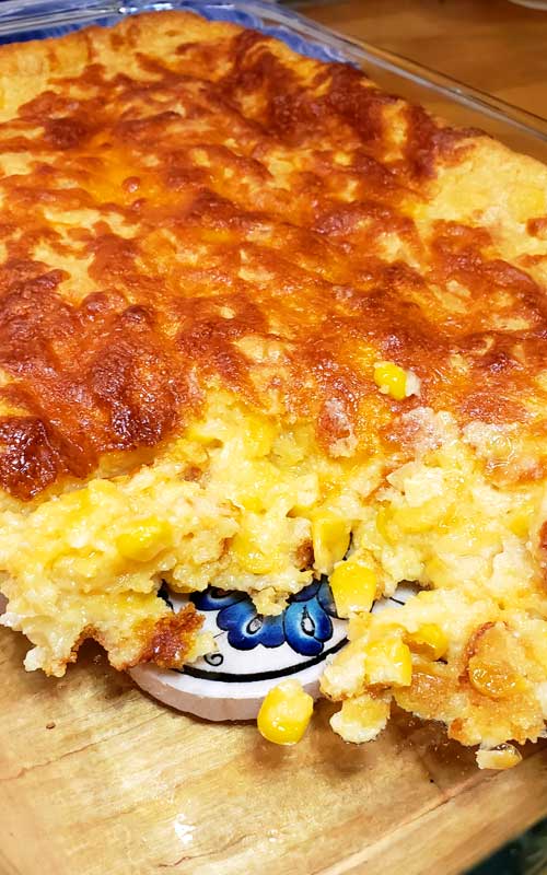 Sweet Creamed Corn Casserole in a glass baking dish with one scoop missing, to show the interior texture.