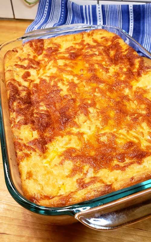 A finished Sweet Creamed Corn Casserole in a glass baking dish, resting on a blue striped towel.