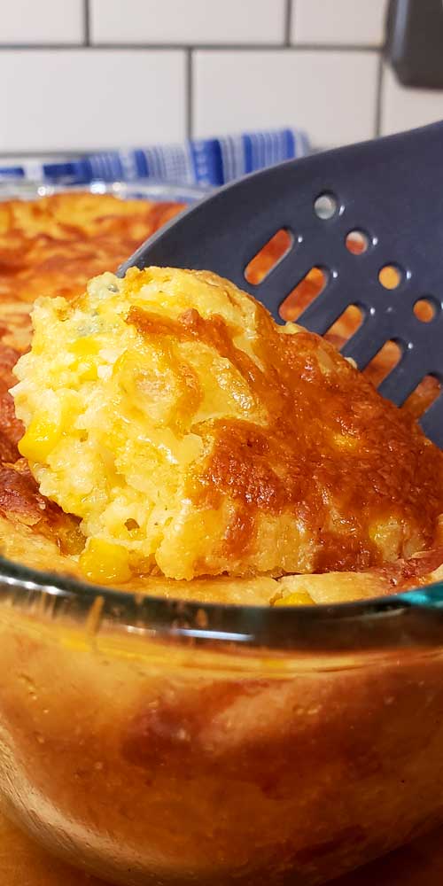 Sweet Creamed Corn Casserole in a glass dish being scooped out with a slotted spoon.