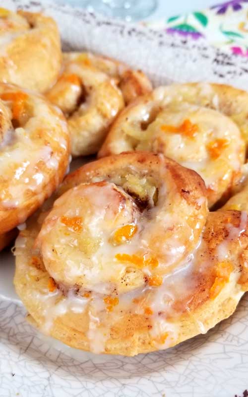 Baked Orange Pineapple Sweet Rolls on a serving platter. Pieces of orange can be seen on the rolls, as well as white icing.