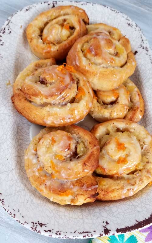 Six finished Orange Pineapple Sweet Rolls on a serving platter. Small pieces of orange and white icing rests on top of each roll.