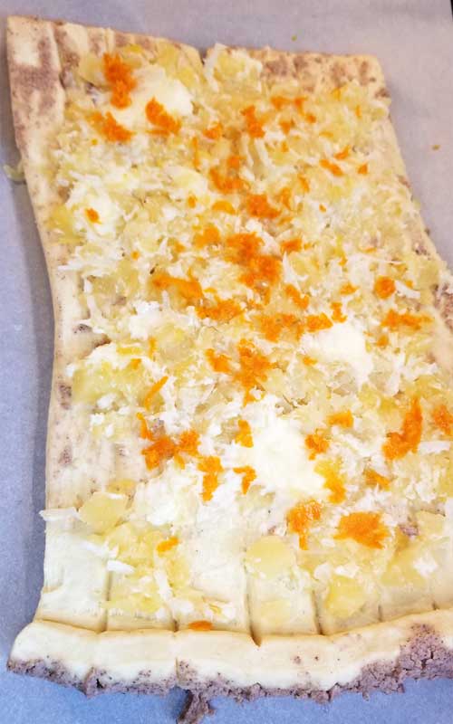 A flattened sheet of dough. The dough is covered in coconut, pineapple, and orange pieces.
