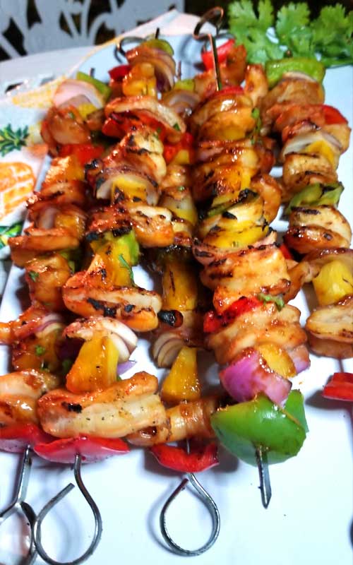 Grilled chicken, bell peppers, onion, and pineapple on metal skewers.