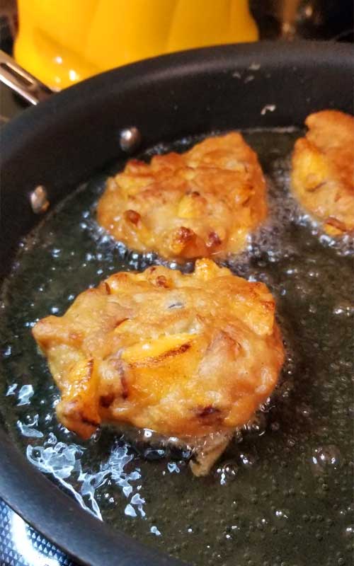 Peach fritters being fried in a black non-stick skillet.