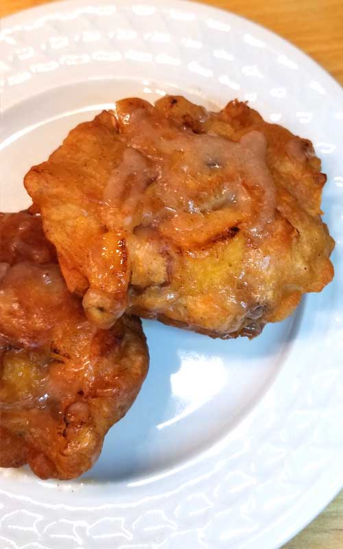 Two peach fritters with no glaze are resting on a white plate.