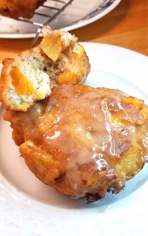 Two Peach Fritters with Honey Cinnamon Glaze on a white plate. One has been split open to show the interior texture.