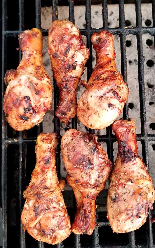 A top down view of six chicken legs on a cast iron grill grate.