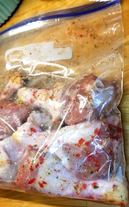Chicken legs being marinated in a zip top bag.