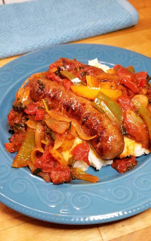 An Italian sausage with peppers and onions served over mashed potatoes, on a blue plate.