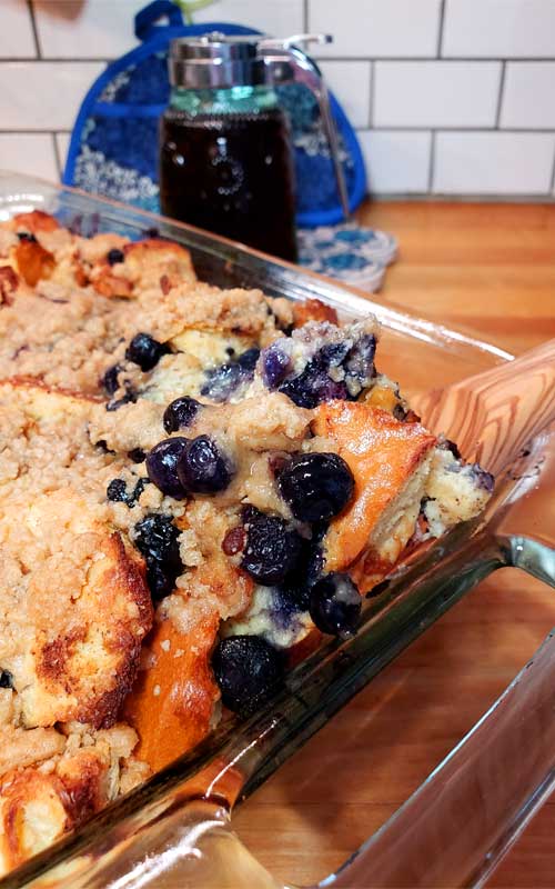 A prepared Easy Blueberry French Toast Casserole with Streusel Topping in a clear glass baking dish.