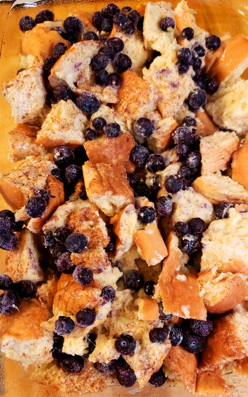 Pieces of bread and blueberries being mixed together.