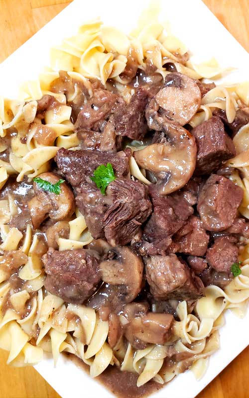 Top-down view on Garlic Butter Beef Tips and Mushroom Gravy over egg noodles on a white plate.