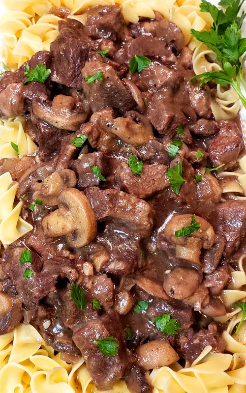 Prime-down gape of Garlic Butter Beef Guidelines and Mushroom Gravy over egg noodles. A dinky bunch of parsley is within the pause ample corner.  Garlic Butter Beef Guidelines and Mushroom Gravy garlic butter beef tips N4