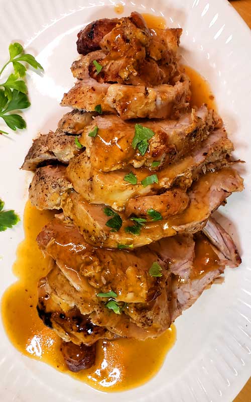 A top down view of a finished and sliced Pork Roast with Brown Sugar Apple Dijon Glaze on a white platter.