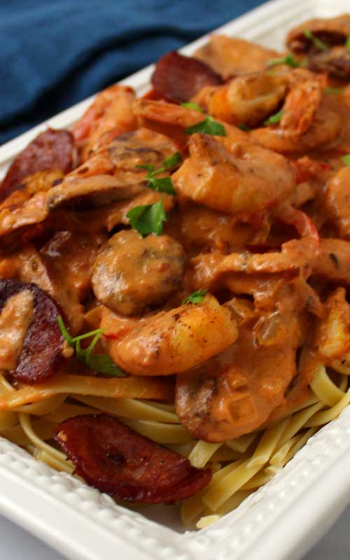 Cream sauce covering a Creamy Cajun Shrimp and Sausage Pasta that is in a white serving platter.
