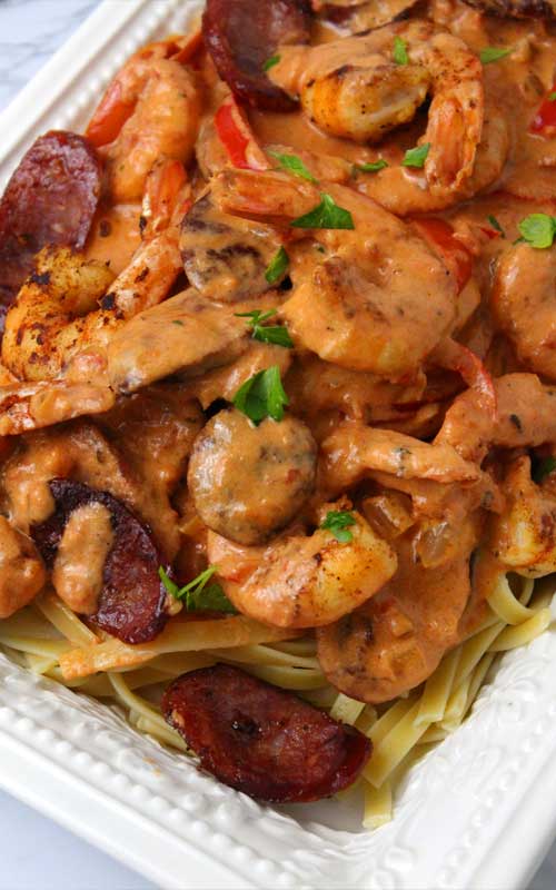 Top down view of a prepared Creamy Cajun Shrimp and Sausage Pasta in a white serving dish. The top is covered in a cream sauce and garnished with parsley.