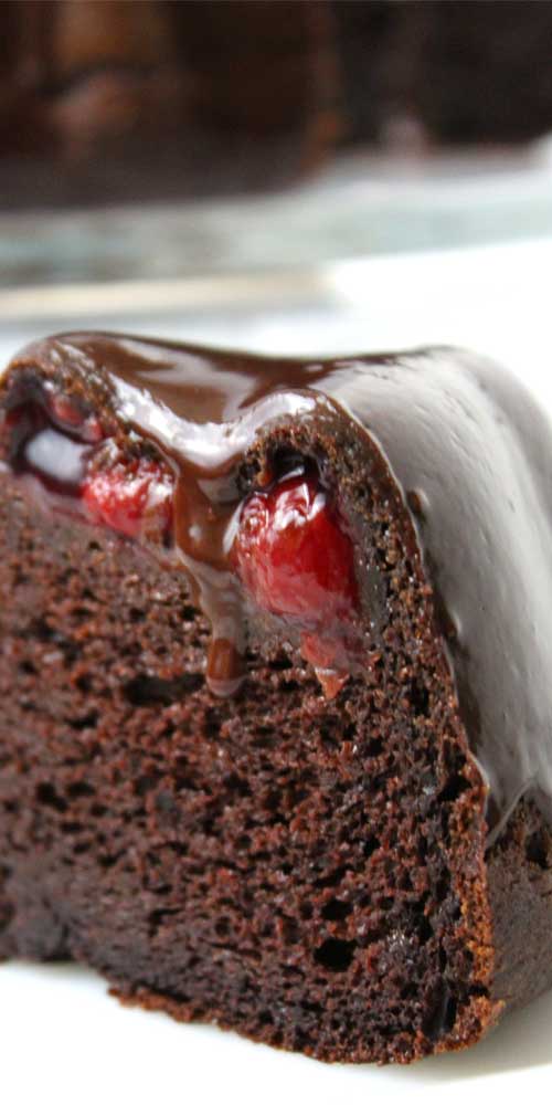 A slice of Chocolate Covered Cherry Bundt Cake on a white plate. The interior texture and cherry filling is visible. The cake is also covered in chocolate ganache.