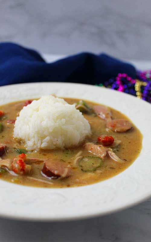 A white bowl has a mound of white rice in the middle, surrounded by an Authentic New Orleans Cajun Gumbo.