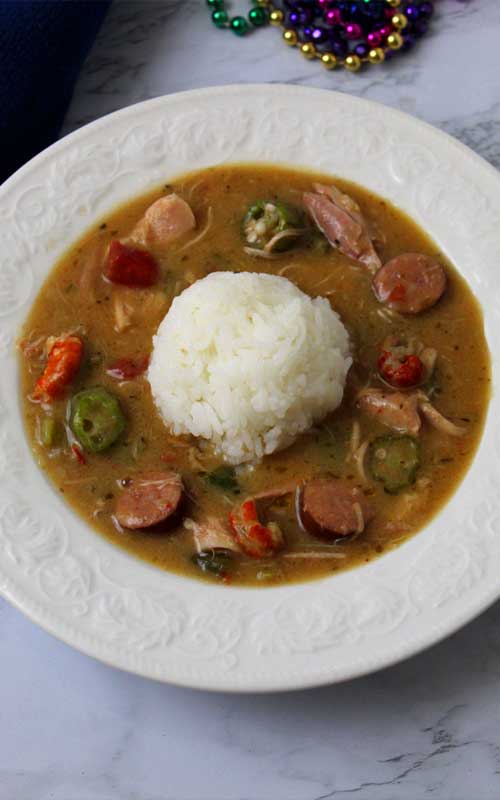 Top down view of a white bowl filled with an Authentic New Orleans Cajun Gumbo and a mound of white rice in the center.