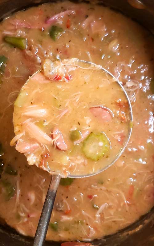 A metal serving spoon scooping some Authentic New Orleans Cajun Gumbo from a pot.