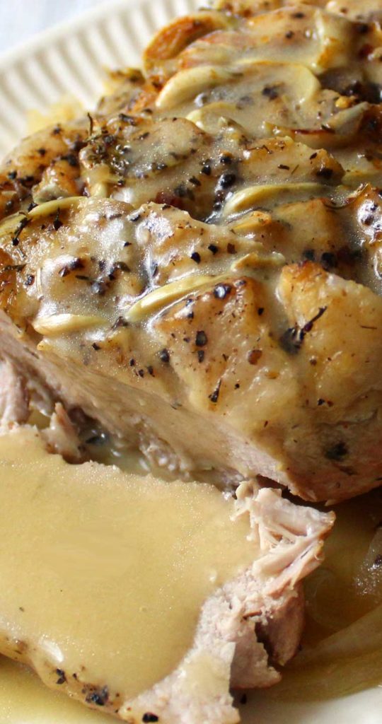 Zoomed in on top of finished recipe for Garlic Herb Pork Roast and Creamy White Wine Gravy. The roast is covered in gravy and sitting on a white plate.