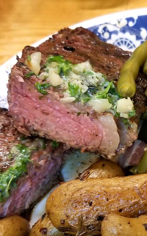 A Grilled Rib-Eye Steak with Roasted Garlic Herb Butter that has been cut open to show that it is cooked medium-rare.