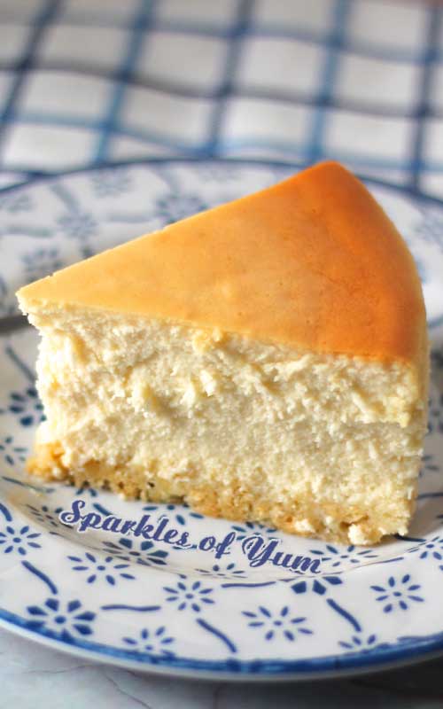 A side view of a slice of New York Cheesecake on a white and blue plate.