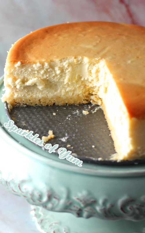 A New York Cheesecake with a quarter of the cheesecake removed. The cheesecake sits on a metal plate, which is on top of a green cake stand.