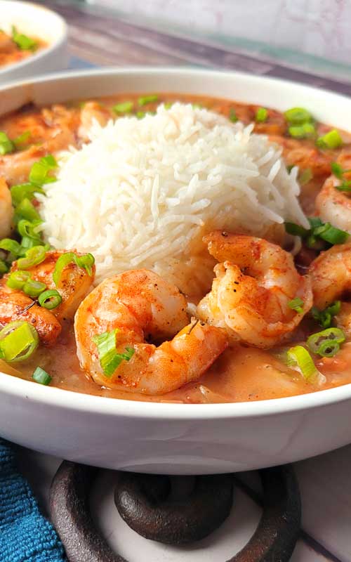 Close up view of shrimp etouffee in a white bowl. The texture of the shrimp and white rice is very visible.