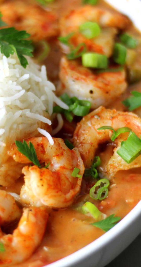 A very close up view of shrimp in a tomato based gravy. A small bit of white rice is on the left edge of the image.